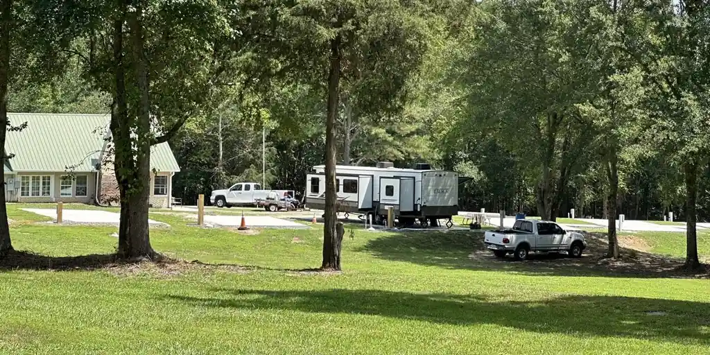Shade trees on the lawn by the bath house, with an RV and trucks parked beyond